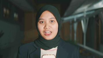 a muslim reporter in a headscarf and a black coat is talking in front of the camera with a smiling face video