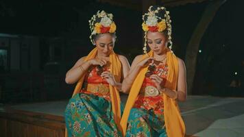 a couple of Indonesian traditional dancers in orange costumes are sitting with their friends in the pavilion video