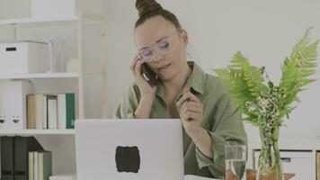a woman in glasses talking on the phone while sitting at a desk video
