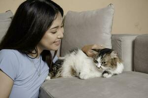 Pretty Asian woman hug a cat and sit on couch with happy emotion. Adorable domestic pet concept. photo