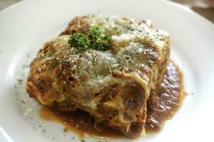 Piece of tasty hot lasagna served with a basil leaf on a white plate. Italian cuisine, menu, recipe. Homemade meat lasagna. Close up, side view photo