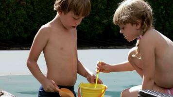 two children playing with a bucket and shovel in a pool video