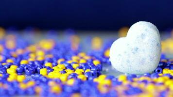 a blue and yellow bead ball sitting on top of a white heart video