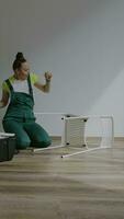 a woman in overalls is sitting on the floor fixing a chair video