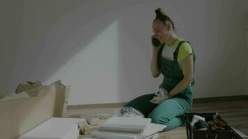 a woman in overalls sitting on the floor answering phone while assembling furniture video