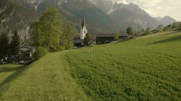 ein Junge und ein Mädchen ist Laufen im das Gras mit ein Kirche im das Hintergrund video