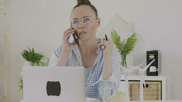 a woman in glasses talking on the phone while sitting at a desk video