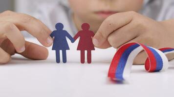 a child holding a paper cutout of two female with a ribbon video