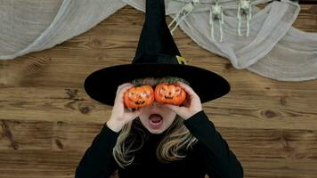 un joven niña en un bruja sombrero participación dos calabazas video