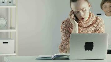 une garçon donnant une fleur à le travail mère séance à une bureau avec une portable video