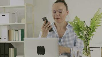 a woman in glasses talking on the phone while sitting at a desk video