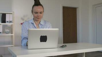 une fatigué femme séance à une bureau en utilisant une portable video