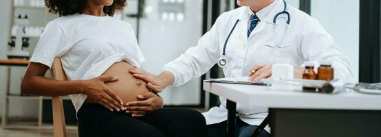 Pregnant african woman has appointment with doctor at clinic. Male gynaecologist OB GYN medic specialist with stethoscope listens to baby's heartbeat in mother's belly. Pregnancy, health care photo