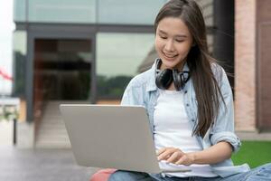 Beautiful Asian woman female student excited checking language test results on laptop. Smile girl happy study online. book in college campus. Portrait female on international Asia University photo
