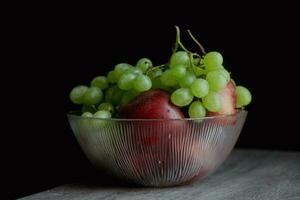 verde uvas manzanas en vaso plato en un oscuro antecedentes. todavía vida fotografía alto calidad foto