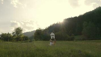 a girl and a boy holding a house cutout sitting in the grass on a hill video