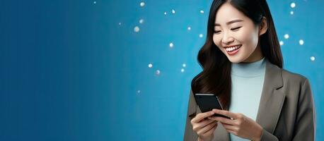 Asian woman using smartphone app messaging on social media pointing away with blue background and copy space for advertisement photo