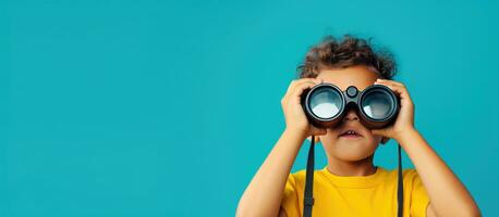 Boy in yellow shirt with binoculars looking on blue background Space for text photo