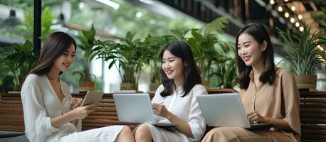 Three attractive Asian females engaged in technology usage and conversation while seated on a caf sofa representing a modern lifestyle and the concept photo