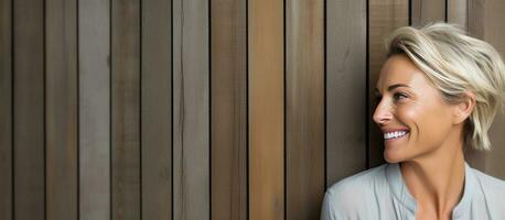 Blonde woman with smile standing near blank space against wooden wall photo