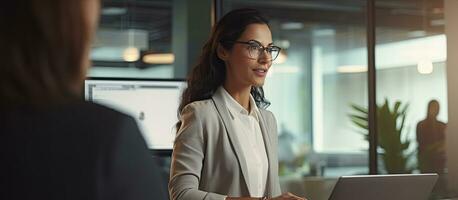 Successful modern businesswoman having a conversation with partner and using laptop in office standing by window photo