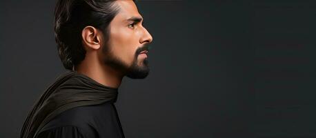 Profile portrait of a young man in traditional Pakistani attire with dark hair mustache and beard against a gray background Horizontal banner with empt photo