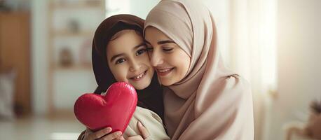 Muslim girl embraces mom with hijab greeting with card and love bonding at home photo