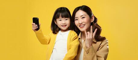 Asian family in casual clothes posing with mobile phone showing blank screen pointing and celebrating on yellow background photo