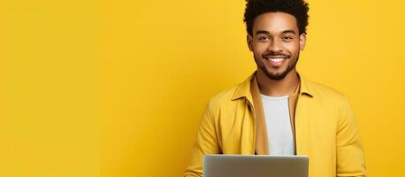 Happy successful African American man freelancer looking at camera with laptop on yellow background photo