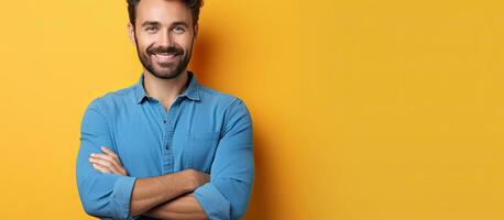 A smiling man in a blue shirt with a beard standing alone on a yellow orange wall background Lifestyle concept Copy space available He is holding his h photo