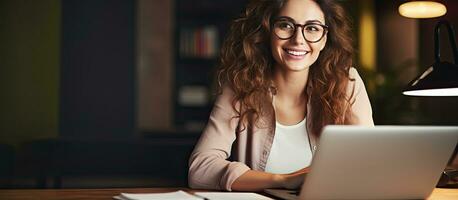 sonriente mujer a escritorio utilizando ordenador portátil y cuaderno estudiando en línea a hogar foto