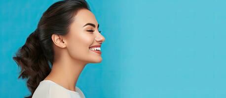Attractive girl smiling in profile portrait with blue background and copy space photo