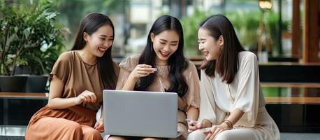Three attractive Asian females engaged in technology usage and conversation while seated on a caf sofa representing a modern lifestyle and the concept photo