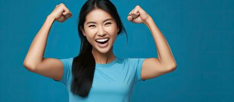 An enthusiastic Asian woman proudly lifting her arms showing off her muscles wearing a blue shirt and smiling photo