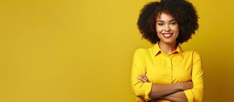 joven africano americano mujer con confidente y sonriente comportamiento posando en amarillo antecedentes cruce brazos en cofre y mantener ojo contacto con California foto