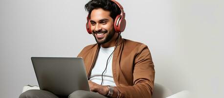 A modern Indian man uses technology to communicate sitting in a white studio with a laptop and headset photo