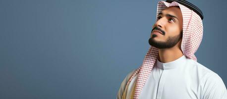 Thoughtful young Arab man daydreaming and looking up against a blank wall photo