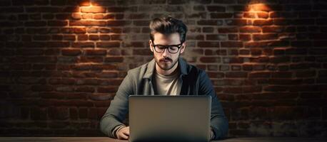 Text space near brick wall young male teacher uses laptop and wears glasses photo