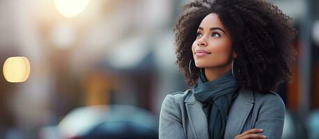 Thoughtful African American woman with crossed arms standing outside looking confident and chic with blurred background and copy space photo