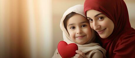 pequeño niña dando madre un regalo corazón dibujado en saludo tarjeta madre vistiendo hijab contento niño abrazando madre y sonriente a el cámara foto