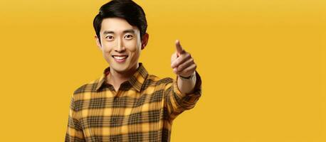 joven atractivo asiático hombre en su 20s sonriente vistiendo un tartán camisa señalando a un anuncio en un amarillo antecedentes representando un estilo de vida concep foto