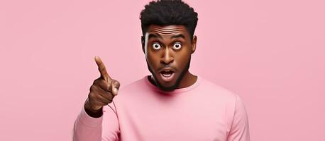 Astonished African American man pointing at empty space expressing surprise and excitement while advertising on pink isolated background photo