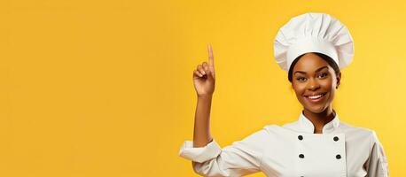 Black female chef smiling and pointing upwards wearing uniform presenting menu on yellow background photo