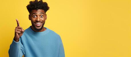 Young attractive black man in blue sweater pointing up at empty space above him on yellow background presenting captivating advertising and enticing deal photo