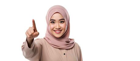 Asian Muslim woman wearing a hijab pointing at copy space on her phone above her isolated on white background photo