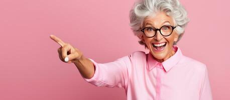 Elderly woman points with two fingers blank space for text Kind looking photo on pink backdrop