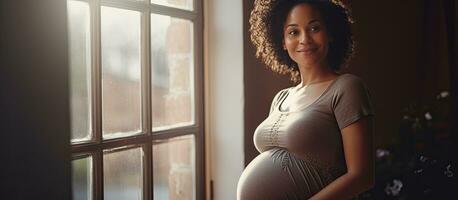Young pregnant black woman smiling and looking at empty space enjoying her pregnancy near a window at home photo