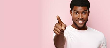 Young African American man in white shirt posing on pastel pink wall pointing fingers Lifestyle idea with empty space photo