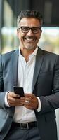 Smiling mature businessman holding smartphone in office using cell phone app for business solutions photo