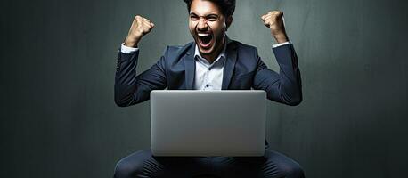 Happy trader using laptop and celebrating success overjoyed man shaking fists cheering big profit photo